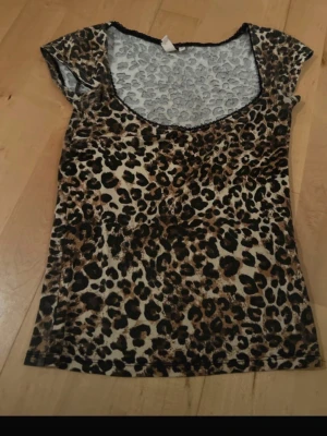Leopardmönstrad topp med kort ärm - Snygg topp med leopardmönster i bruna och svarta toner. Modellen har korta ärmar och rundad urringning. Materialet känns mjukt och stretchigt, troligen polyester. Perfekt för dig som vill sticka ut med ett djurmönster.