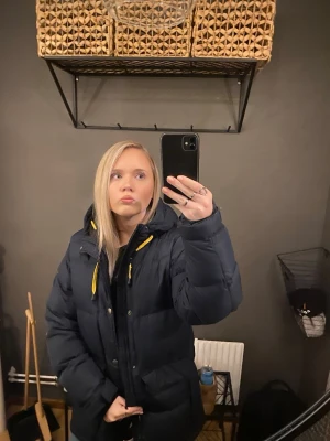 vinter jacka - Snygg mörkblå pufferjacka med huva och gula dragkedjedetaljer. Jackan har en quiltad design och stora fickor framtill. Perfekt för kalla dagar och ger en cool vibe. storlek xxs men är passar mig som är xs/s. väldigt bra skick och väldigt varm, däremot lossnar de någon fjäder på insidan men inte ofta alls. lägg prisförslag!