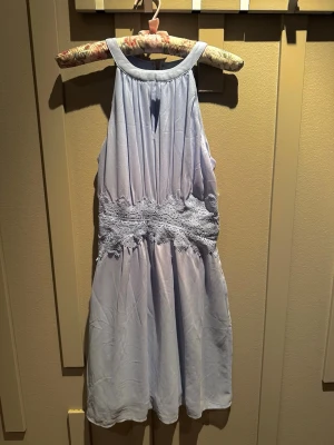 Ljusblå klänning från Vila - Supersöt ljusblå  klänning från Vila med spetsdetaljer i midjan och halterneck. Klänningen har en mjuk, flowy känsla och stängs med dragkedja i ryggen. Perfekt för sommarens alla tillfällen!