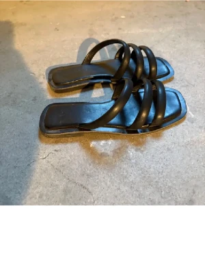 Svarta sandaler med breda remmar - Stilrena svarta sandaler med tre breda, vadderade remmar och fyrkantig tå. Snygg minimalistisk design som passar till många outfits. Tillverkade i ett material som liknar skinn. Använt fåtal gånger. Köpta i köpenhamn för 300kr!