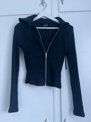 Marinblå ribbad hoodie med dragkedja - Säljer en marinblå ribbad hoodie från GINA TRICOT med dragkedja framtill och långa ärmar. Hoodien har en åtsittande passform och huva med dragsko. Perfekt till ett par jeans eller kjol för en chill look.