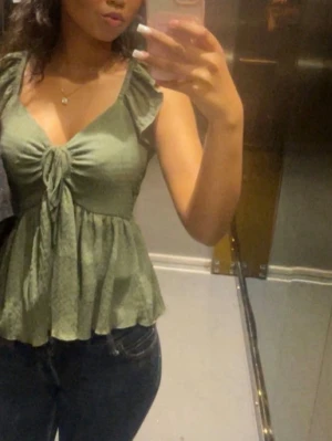 Grön linnetopp med knyt framtill - Snygg grön linnetopp med knyt framtill och v-ringning. Toppen har en luftig passform och är ärmlös, perfekt för varma dagar.