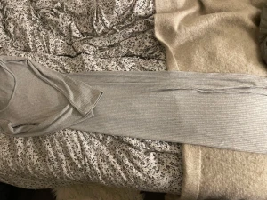 Lång ribbad grå klänning - Säljer en lång, ribbad klänning i ljusgrått med lång ärm och rundad urringning. Klänningen har en kroppsnära passform och är tillverkad i ett mjukt, stretchigt material som känns bekvämt mot huden. Perfekt för dig som gillar stilrena och enkla plagg.