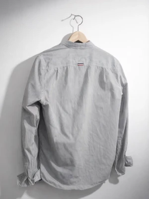 Randig skjorta från Superdry - Klassisk långärmad skjorta från Superdry med tunna vertikala ränder i vitt och grått. Skjortan har knappar framtill, bröstficka och en liten logotypdetalj på ryggen. Perfekt för en avslappnad men stilren look.