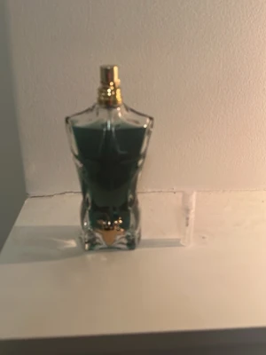 Jean Paul Gaultier Le beau parfym - En ikonisk parfymflaska formad som en manlig torso från Jean Paul Gaultier. Flaskan är i glas med blågrön vätska och har detaljer i guld på korken. Perfekt för dig som gillar unika och snygga flaskor i badrumshyllan.