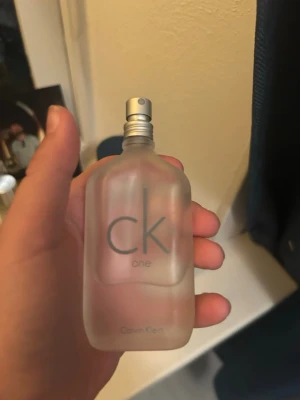 CK One parfym från Calvin Klein - Minimalistisk parfymflaska i frostat glas med silverfärgad spraykork. Klassisk unisexdoft från Calvin Klein, CK One, med enkel och stilren design. Perfekt för dig som gillar fräscha och lätta dofter. Använd 50%. 