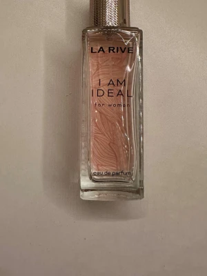 La Rive I Am Ideal Eau de Parfum - La Rive I Am Ideal Eau de Parfum för kvinnor i en elegant, rektangulär glasflaska med ljusrosa doftvätska och ett stilrent mönster på insidan. Flaskan har en silvrig kork med struktur och modern design. Ca 35ml kvar