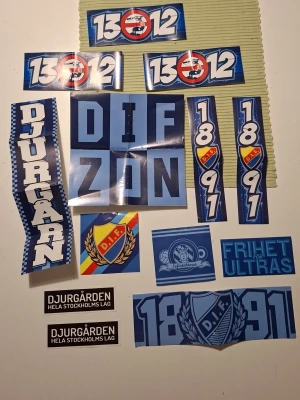 Djurgården klistermärken  - Ett paket med flera olika klistermärken från Djurgårdens IF i blå, vit, svart och gul färg. Motiven inkluderar DIF-loggan, text som 'Djurgården', '1312', '1891', 'Frihet för ultras' och andra supporterbudskap. Perfekt för att visa ditt stöd för laget.