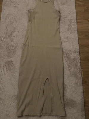 Beige ribbad långklänning Gina Tricot - Ribbad beige långklänning från Gina Tricot med ärmlös design och rund halsringning. Klänningen har en slits framtill och är figurnära i modellen. Perfekt för dig som älskar de mer basic.