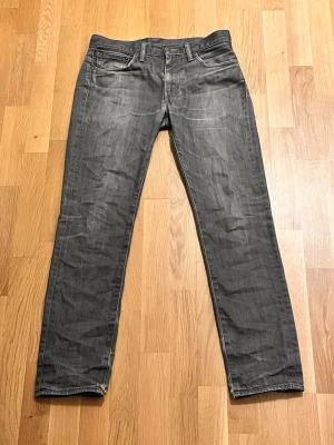 Grå Levis jeans straight fit - Snygga grå jeans från Levis med klassisk femficksdesign och raka ben. Jeansen har en diskret tvättad look och Levis ikoniska röda etikett på bakfickan. Perfekta för en avslappnad och stilren outfit. W32 L32. 