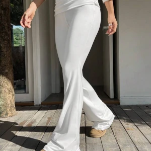 Vita bootcut byxor i mjukt tyg - Säljer ett par vita bootcut byxor med hög midja och snyggt fall. Byxorna är gjorda i ett mjukt och stretchigt material som sitter skönt och ger en clean look. Perfekta för dig som gillar en stilren och trendig vibe.