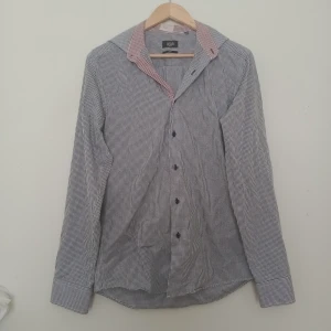 Rutig skjorta från Long Island, slim fit - Snygg rutig skjorta från Long Island i slim fit-modell. Skjortan har blåvitt rutmönster med kontrastkrage i rödvitt, långa ärmar och knappar framtill. Perfekt för dig som gillar klassisk men ändå modern stil.