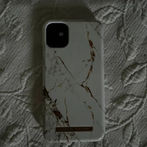 Vit marmormönstrad mobilväska Ideal of Sweden till iPhone 11 - Snyggt mobilskal till iPhone 11 från Ideal of Sweden i vit med marmormönster och gulddetalj. Stilren design som ger din mobil en lyxig touch. Passar perfekt för dig som vill ha en trendig och praktisk accessoar. Pris kan diskuteras.