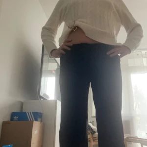 Svarta kostymbyxor från Vero Moda - Svarta kostymbyxor från Vero Moda med klassisk rak passform och hög midja. Byxorna har dragkedja och knappstängning framtill och är tillverkade i ett mjukt, vävt material som känns skönt mot huden. Perfekta för en clean och stilren look.