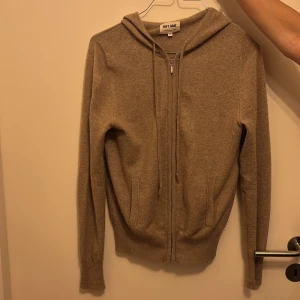 Beige hoodie i kashmir från Soft Goat - Mysig beige hoodie från Soft Goat i 100% kashmir. Tröjan har dragkedja framtill, huva med snörning och två fickor. Perfekt för dig som gillar en chill och lyxig stil. Långärmad och supermjuk – ett måste i garderoben!