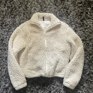 Vit teddyjacka från H&M Divided XS - Mysig vit teddyjacka från H&M Divided i storlek XS. Jackan har dragkedja framtill, hög krage och är tillverkad i fluffigt teddy-material. Perfekt för kyliga dagar när du vill vara både varm och snygg.