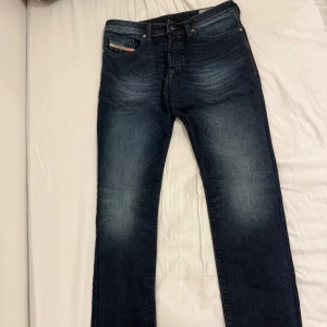 Säljer Mörkblå Diesel Jeans! - Har endast använt 1 gång. Storlek: W:28. L:32. Snygga mörkblå jeans från Diesel med klassisk femficksdesign och diskreta slitningar framtill. Jeansen har raka ben och normal passform, perfekt för en avslappnad stil. Tidlös tvätt och detaljerade sömmar på bakfickorna.