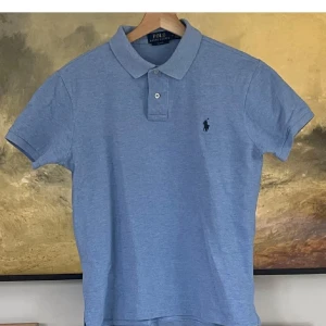Blå pikétröja Polo Ralph Lauren M - Snygg ljusblå pikétröja från Polo Ralph Lauren i slim fit-modell. Klassisk krage med två knappar och broderad logga på bröstet. Tillverkad i mjuk bomull, perfekt för en clean och stilren look.