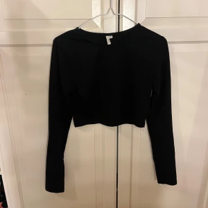 Svart croppad långärmad topp - En stilren svart croppad topp från Nelly med lång ärm och rund hals. Perfekt att matcha med höga jeans eller kjol för en clean look. Mjuk och skön bomull som sitter snyggt och enkelt.