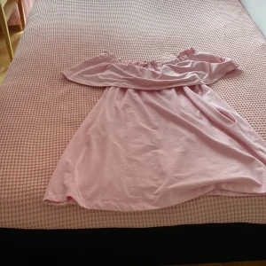 Rosa offshoulder klänning H&M - Söt ljusrosa kortklänning från H&M med offshoulder-modell och volang upptill. Klänningen har en avslappnad passform och är tillverkad i mjuk bomull, perfekt för varma dagar. Enkel och stilren design som ger en fräsch look.