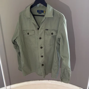 Grön overshirt från Ralph Lauren - Snygg ljusgrön overshirt från Polo Ralph Lauren i klassisk passform. Skjortan har två bröstfickor med knappar, raka linjer och långa ärmar. Perfekt lager-på-lager-plagg med stilren look och robust känsla skick 8/10 .