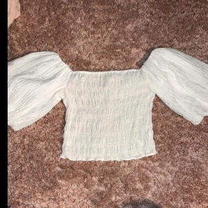 Vit offshoulder topp med puffärm - Superfin vit offshoulder topp med bred smockad kropp och stora puffiga ärmar. Tunt, lätt material som ger en luftig känsla och trendig look. Perfekt att styla med jeans eller kjol för en cool vibe.