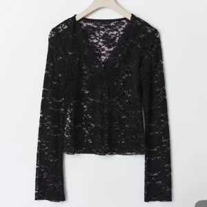 Svart spetsblus med v-ringning - Säljer en svart långärmad blus i genombruten spets med v-ringad hals. Toppen har en feminin och elegant look med transparenta ärmar och kropp. Perfekt att styla med jeans eller kjol för en cool vibe.