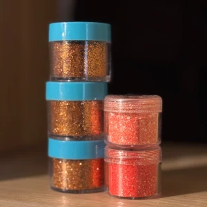 5 pack glitter till naglar  - 5 små burkar med löst glitter i orangea toner till naglar. Kommer i genomskinliga plastburkar med blå och klara lock. Burkarna kan ha repor pga att ha legat bland andra produkter och märkta med något nummer, men det är inga problem med produkterna. 