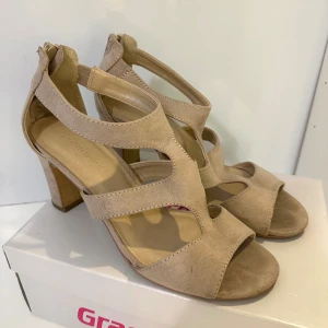 Beige sandaler med klack - Snygga beige sandaler från Dinsko med öppen tå och klack. Skorna har breda remmar i mockaimitation och dragkedja bak för enkel påtagning. Perfekta för dig som vill ha en stilren och trendig look till sommaren.