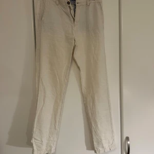 Beiga linnebyxor från Kappahl W30 L32 - Snygga beiga linnebyxor från Kappahl med klassisk rak passform. Byxorna har sidfickor, bakfickor med knapp och ett stilrent, ljust tyg. Perfekta för en chill och stilren look under varmare dagar. Byxorna har två små fläckar på höger backben. 