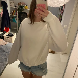 Vit oversized sweatshirt - Enkel och stilren vit sweatshirt med oversized passform och långa ärmar. Tröjan har rund halsringning och breda muddar vid ärmslut och nederkant. Perfekt för en chill och avslappnad look.