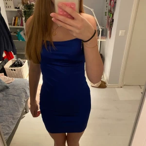 Marinblå tight kort klänning - Säljer en marinblå kort klänning med smala axelband som korsas i ryggen. Klänningen är figurnära och har en enkel, stilren design med slät yta. Perfekt för dig som gillar minimalistisk och trendig stil.
