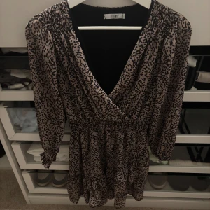 Leopardmönstrad omlottklänning Vero Moda - Snygg kort leopardmönstrad omlottklänning från Vero Moda med v-ringning och resår i midjan. Klänningen har trekvartsärmar och är tillverkad i ett lätt, luftigt material som ger en skön känsla.