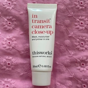 Thisworks in transit camera close-up primer - En multifunktionell primer från Thisworks som även fungerar som ansiktsmask och fuktkräm. Kommer i en vit tub med röd och svart text, Perfekt för att skapa en jämn bas innan sminket.