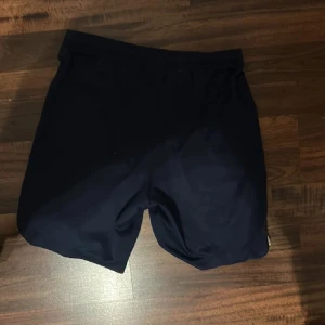 Mörkblå PSG Dri-Fit shorts från Nike - Snygga mörkblå PSG shorts från Nike med Dri-Fit teknologi. De har elastisk midja och är tillverkade i lätt polyester som andas. På framsidan finns både Nike-logga och Paris Saint-Germain klubbmärke. Perfekta för fotboll eller träning. Hör av er vid frågor eller funderingar:)