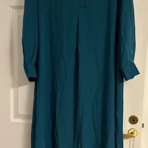 Turkos långklänning från Shein Curve  - Säljer en stilren turkos långklänning från Shein Curve i storlek 0XL. Klänningen har lång ärm med knapp vid manschetten. Materialet känns lätt och smidigt, perfekt för dig som gillar minimalistisk look.