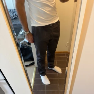 Mörkgrå chinos med normal passform - Säljer ett par stilrena mörkgrå chinos med klassisk rak passform. Byxorna har sidfickor och knappgylf, perfekta till både skjorta och t-shirt. Materialet känns mjukt och bekvämt, och färgen är lätt att matcha med det mesta.
