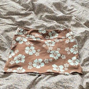 Brun blommig kortkjol med mintmönster - Supersöt kortkjol i brun med stora mintgröna blommor. Kjolen har en rak passform och är perfekt för dig som gillar en lekfull och trendig stil. Mjuk och stretchig känsla, passar perfekt till sommaren.