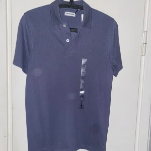 Blå pikétröja från Jack & Jones - Snygg blå pikétröja från Jack & Jones med klassisk krage och två knappar framtill. Perfekt för en clean och stilren look.