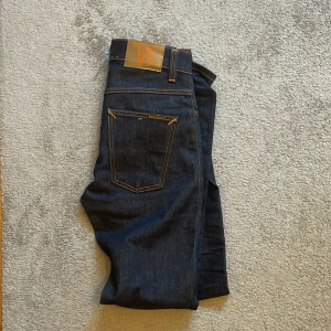 Mörkblå jeans från Nudie Jeans - Snygga mörkblå jeans från Nudie Jeans. Jeansen är endast använda ett fåtal gånger och är i nyskick. Nypriset ligger på 1400. Storleken är 29w 32L. Skriv även ifall du har en fråga