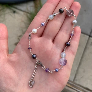 Lila och vit pärlarmband med stenar - Unikt armband med blandade pärlor och stenar i lila, vitt och silver. Kedja och detaljer i silverfärgad metall, med pärlor i olika former och storlekar. Snyggt att matcha med andra smycken för en personlig vibe. Justerbar längd med kedja och lås.