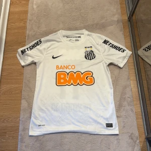 Vit Santos Neymar Jr fotbollströja Nike - Santos FC fotbollströja i vitt med Neymar Jr och nummer 11 på ryggen. Tröjan har korta ärmar, svarta tryck och orangea sponsorloggor. Den är i storlek Medium för män, skriv vid funderingar och annat behöver få den såld eftersom den är förliten för mig