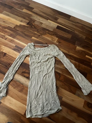 Beige långärmad stickad topp - Säljer en beige långärmad stickad topp med ribbad struktur och spetsdetaljer vid ärmslut och nederkant. Toppen har en något vid halsringning och är figurnära i modellen. 