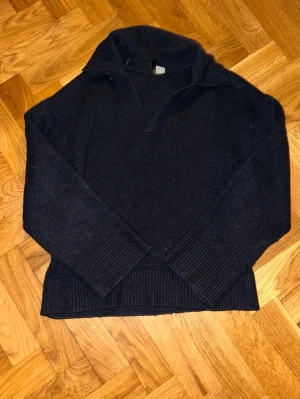 Mörkblå stickad tröja från Monki - Säljer en mörkblå stickad tröja från Monki med krage och v-ringad hals. Tröjan har långa ärmar och breda ribbade muddar vid ärmslut och nederkant. Perfekt för dig som gillar en chill och stilren look.