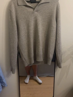 Grå ulltröja från Massimo Dutti - Säljer en stilren grå tröja från Massimo Dutti i 100% ull. Tröjan har krage, v-ringad öppning och långa ärmar. Perfekt för dig som gillar klassisk och enkel design med en mjuk känsla. Passar till många olika outfits.