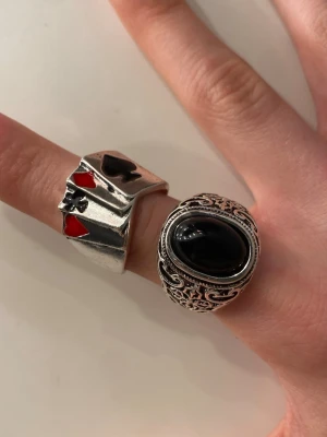 Två statement ringar - Bilderna visar två ringar, båda i ej äkta silver. En har en stor svart pärla och den andra efterliknar kort. Ena ringen är justerbar. Styckpris 12kr, båda för 20kr!