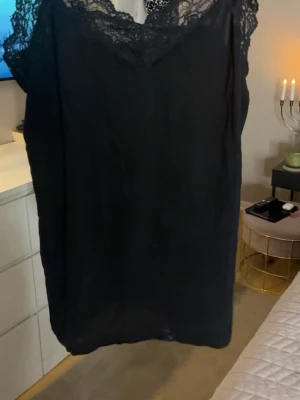 Svart spetslinne från Object - Säljer ett svart linne  från Object med vacker spets upptill och v-ringad hals. Linnet  är ärmlös och har en enkel, rak passform som ger en stilren look. Perfekt för dig som gillar klassiska detaljer och svart färg.