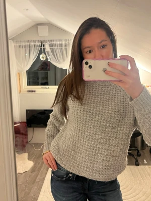 Grå stickad tröja med grov struktur - Mysig grå stickad tröja med grov struktur och rund hals. Tröjan har lång ärm och en lite loose passform, perfekt för kyliga dagar. Enkel och stilren design som är lätt att matcha med jeans eller kjol.