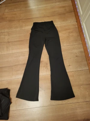Svarta bootcut tajts - Säljer ett par svarta bootcut byxor.  Byxorna har en snygg utsvängd passform och är gjorda i ett stretchigt material som sitter skönt. Perfekta för dig som gillar en stilren och trendig look.