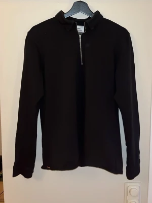 Svart half zip tröja från Ciszere - Svart långärmad tröja från Ciszere i slim fit med krage och half zip-dragkedja framtill. Stilren design utan mönster, perfekt för dig som gillar minimalistiskt och cleant. Materialet känns mjukt och bekvämt mot huden. Det är en storlek L slim men passar mer storlek M